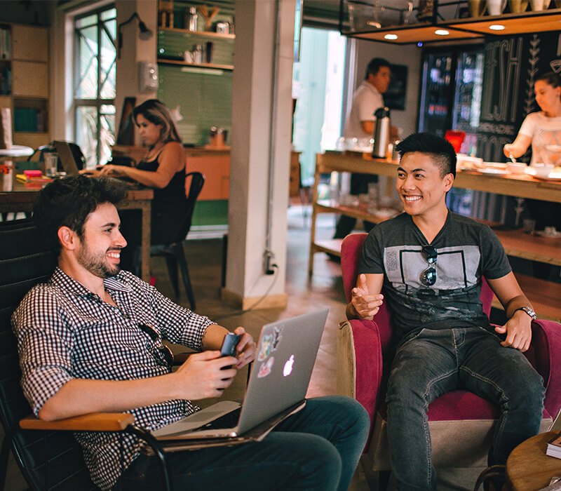 Two people talking through a project over a laptop in a bright cafe