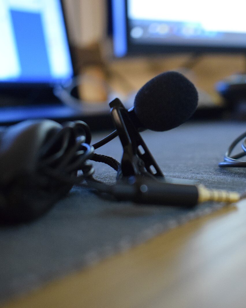 A clip-on lavalier microphone and its cable resting on a desk beside a laptop, ready to run to the recording device